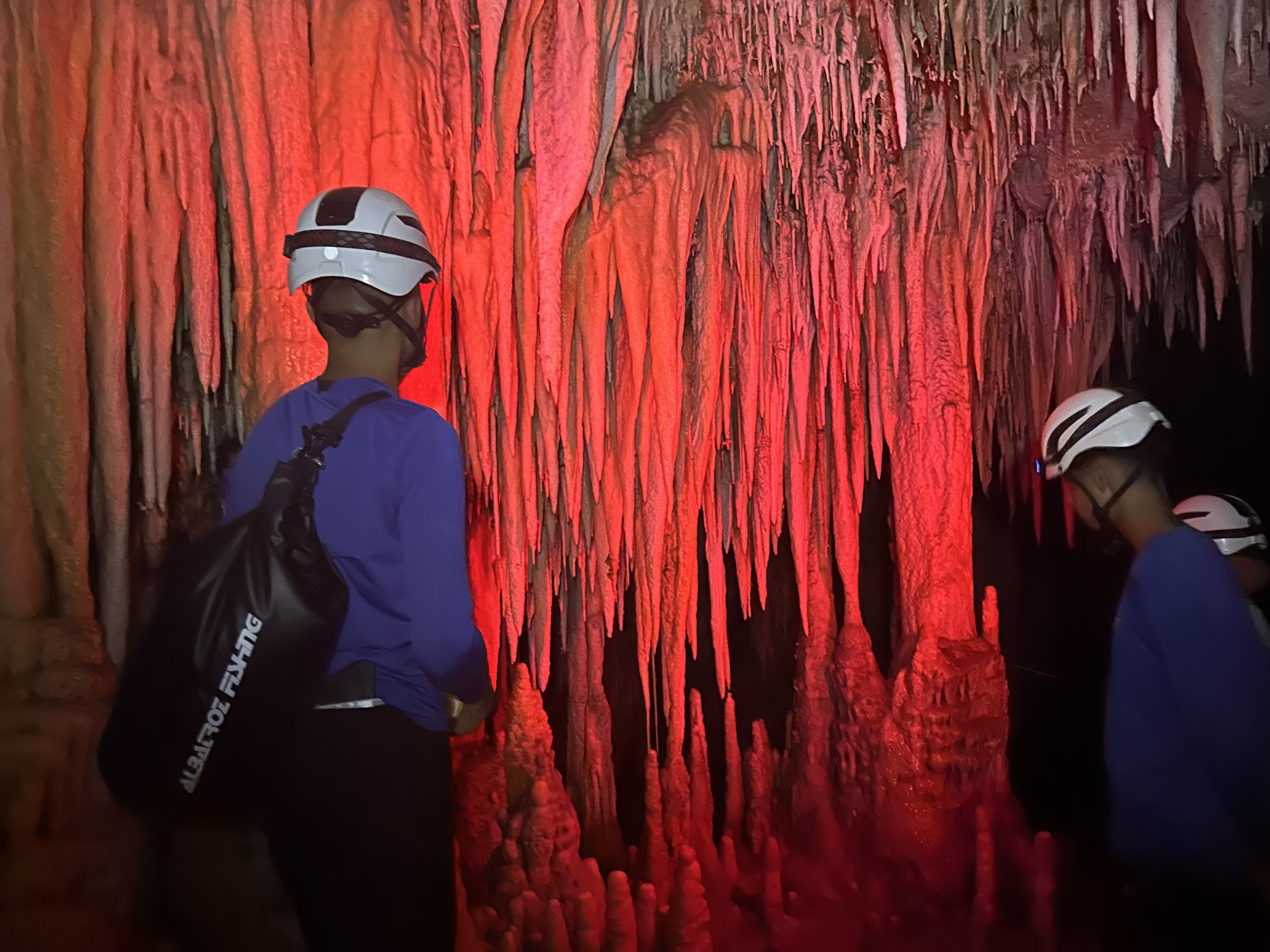 Exploradores observando parede com estalactites em vermelho